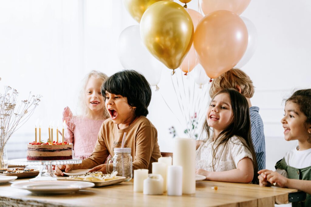 kids budget party - kist sat at a party table with balloons behind them.