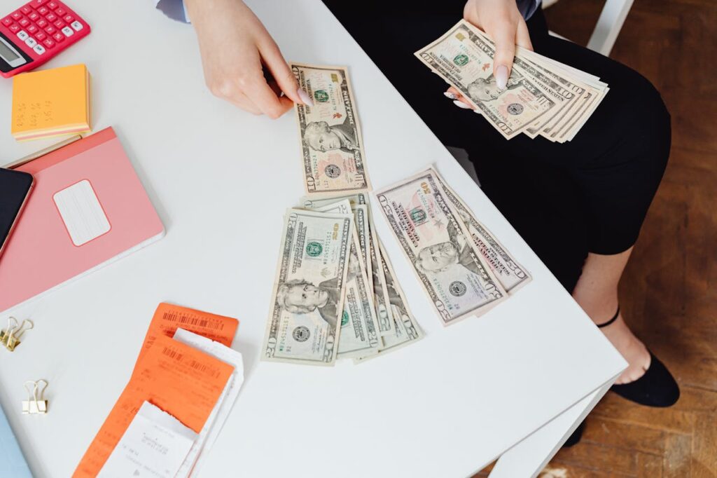 High-Angle Shot of a Person Counting Paper Money on White Table
